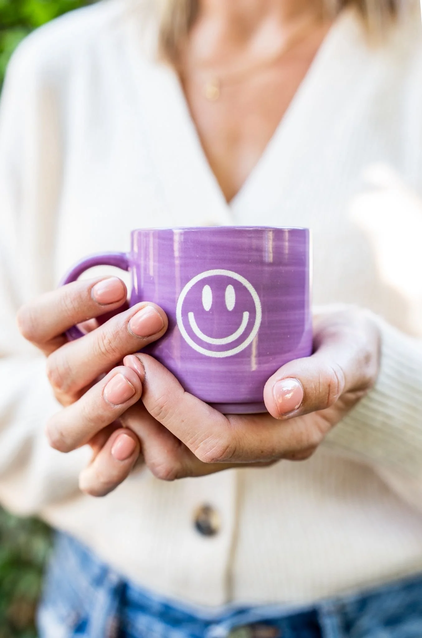 A woman holding a purple mug with a white smiley face design.
