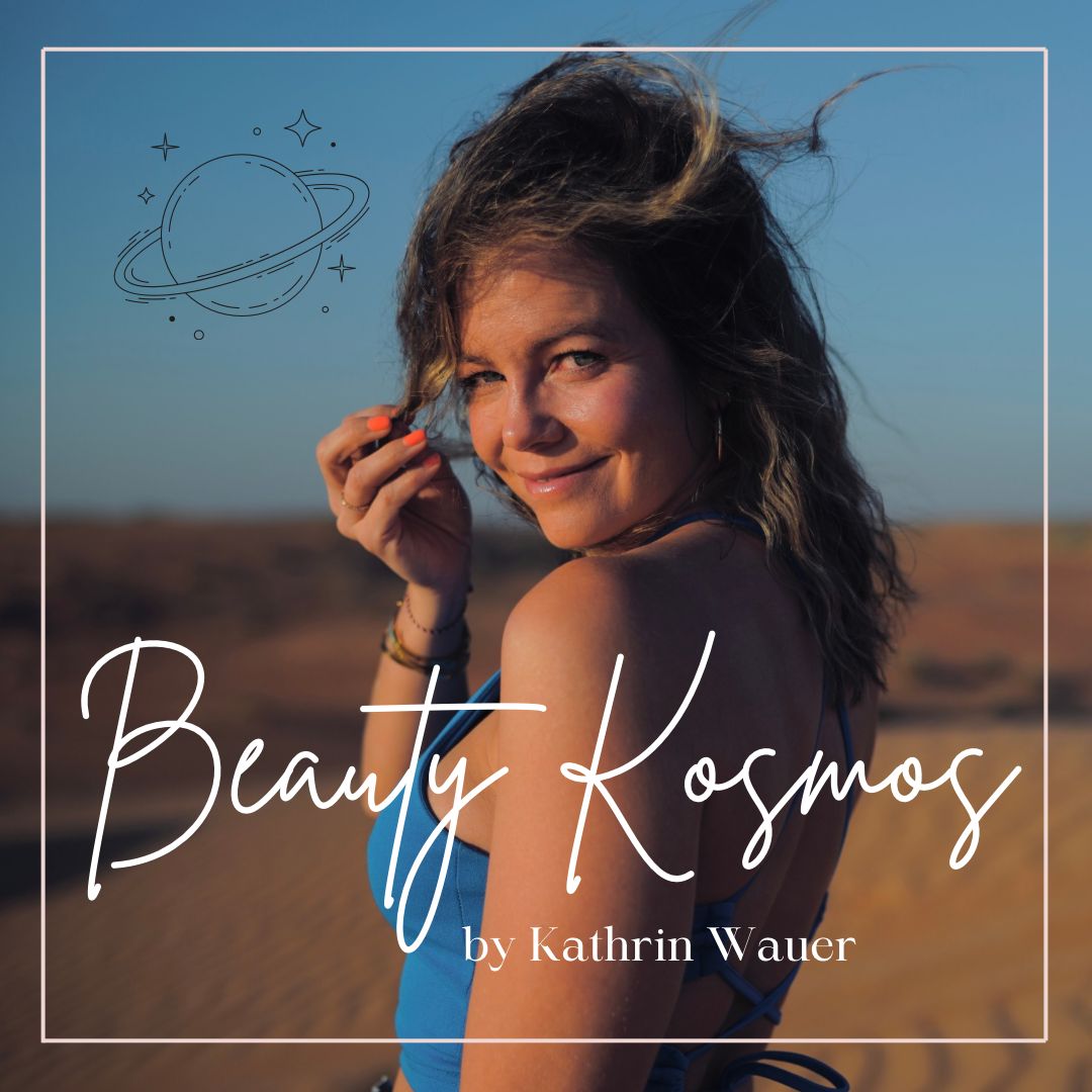 Eine Frau mit lockigem Haar trägt ein blaues Top und steht in einer Wüstenlandschaft mit blauem Himmel. Es ist Sonnenuntergang. Über ihrem Kopf schwebt eine handgezeichnete Darstellung eines Planeten mit Sternen, und auf dem Bild steht der Text 'Beauty Kosmos von Kathrin Wauer'.