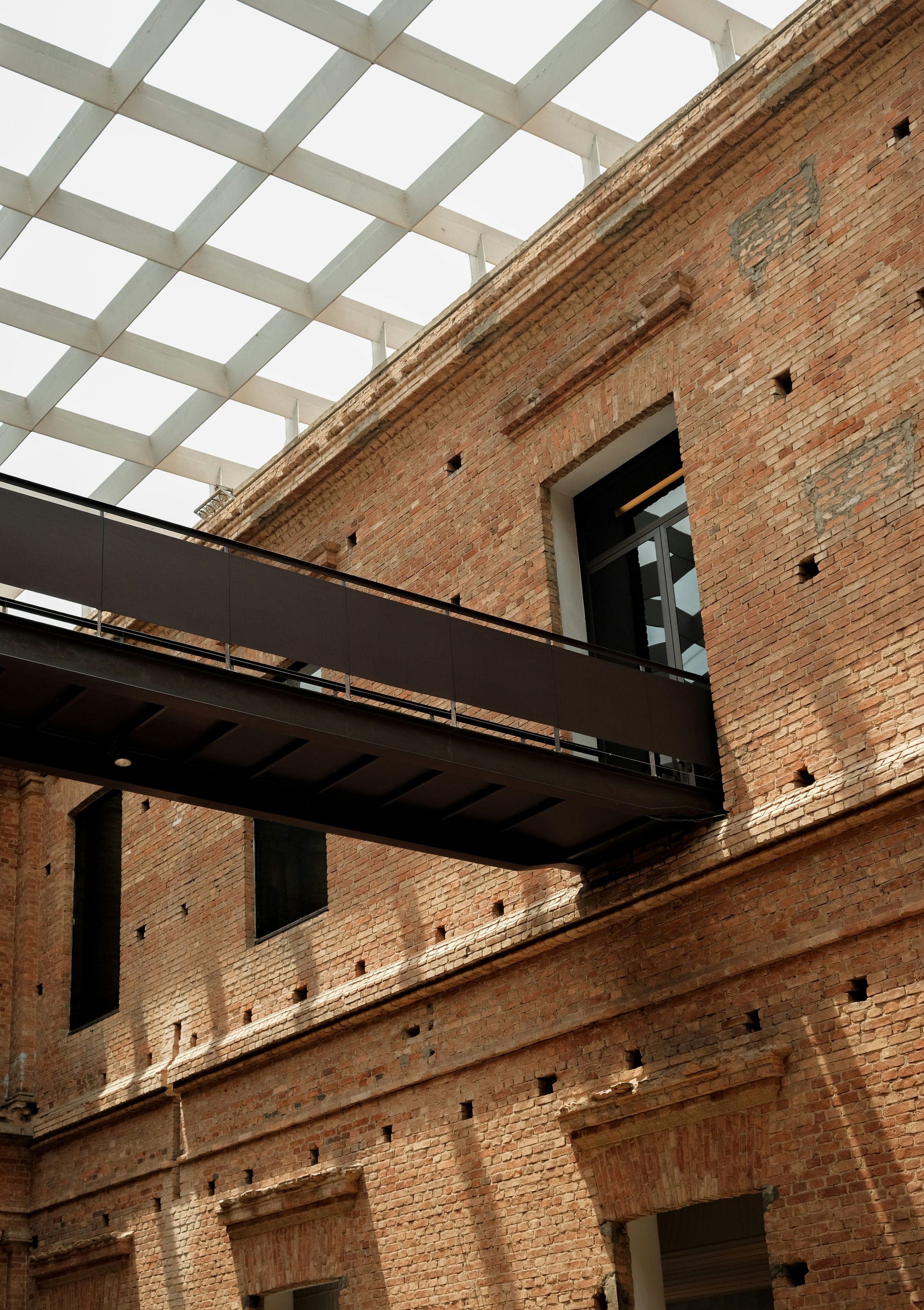 Interior view of a brick building with a modern metal bridge and a glass ceiling structure overhead.