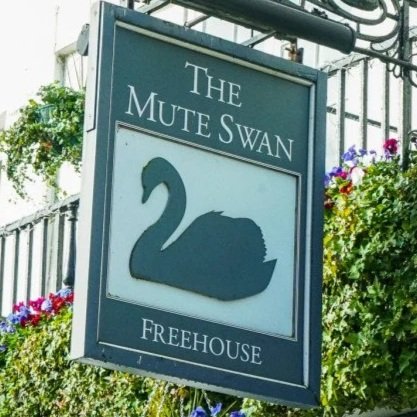 Sign for The Mute Swan Freehouse pub with a black swan icon on a teal background, surrounded by flowers and greenery.