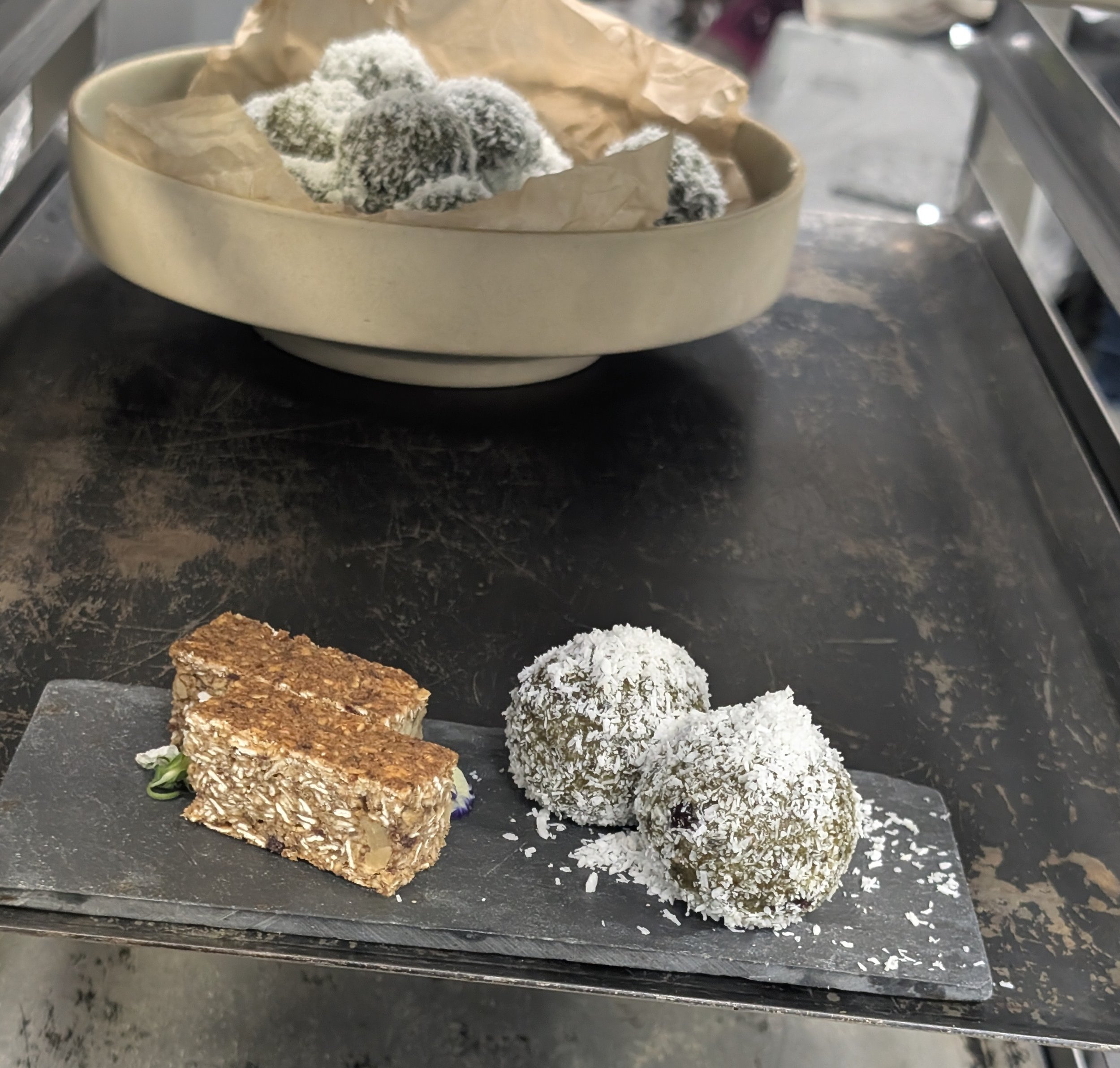 Two energy bites coated with shredded coconut and a granola bar on a gray rectangular plate.