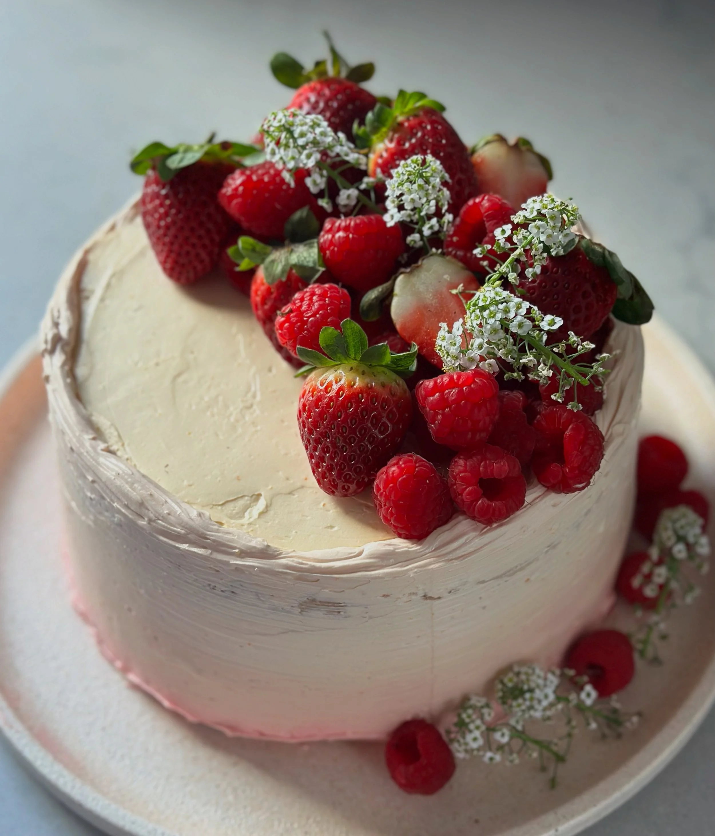 A round cake topped with strawberries, raspberries, small white flowers, and green leaves
