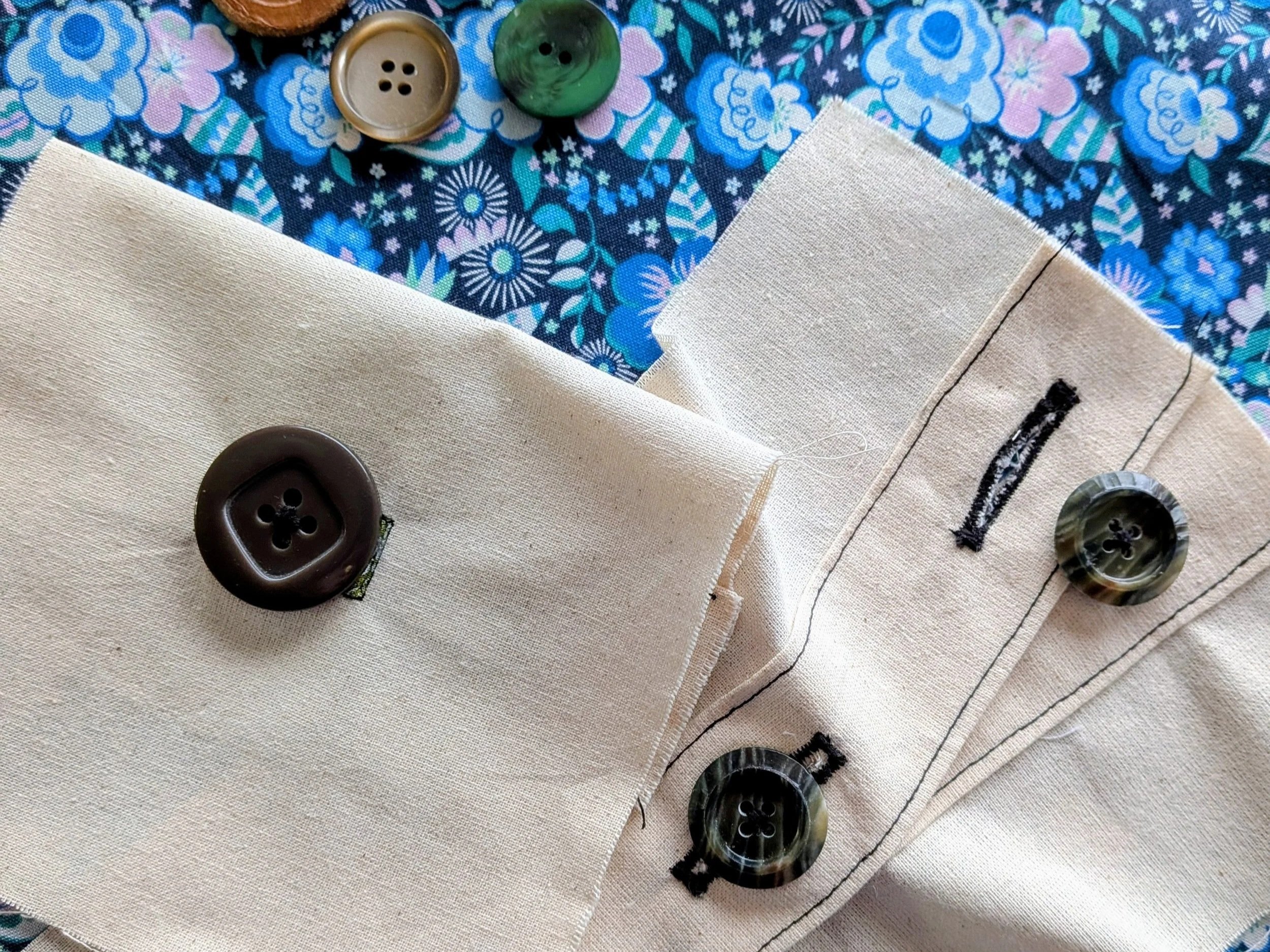 Two calico samples show buttons and buttonholes neatly sewn in black thread. They sit in front of a blue floral background with a scattering of loose buttons near the top of the image.