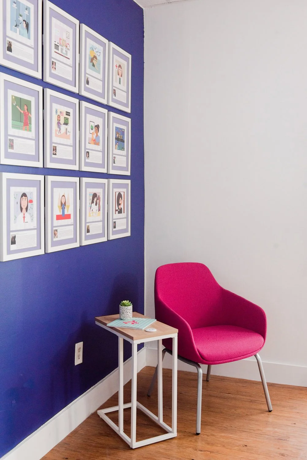 Pink armchair and side table against a navy wall with framed prints