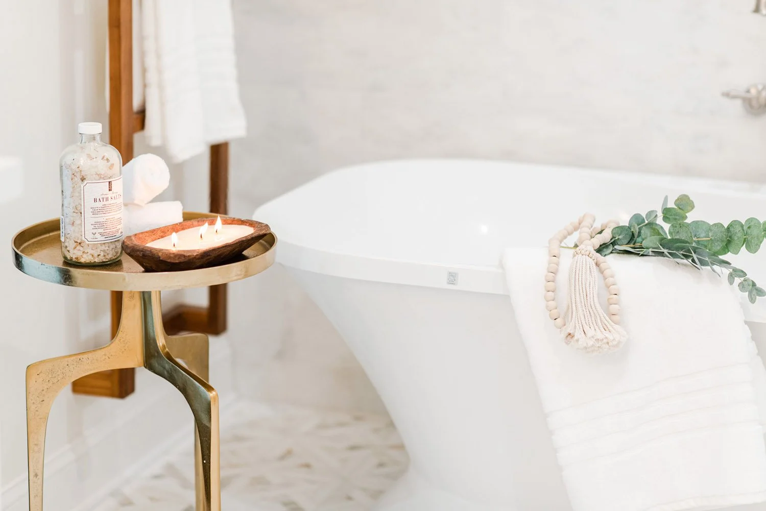 Brass side table with bath accessories beside a freestanding tub