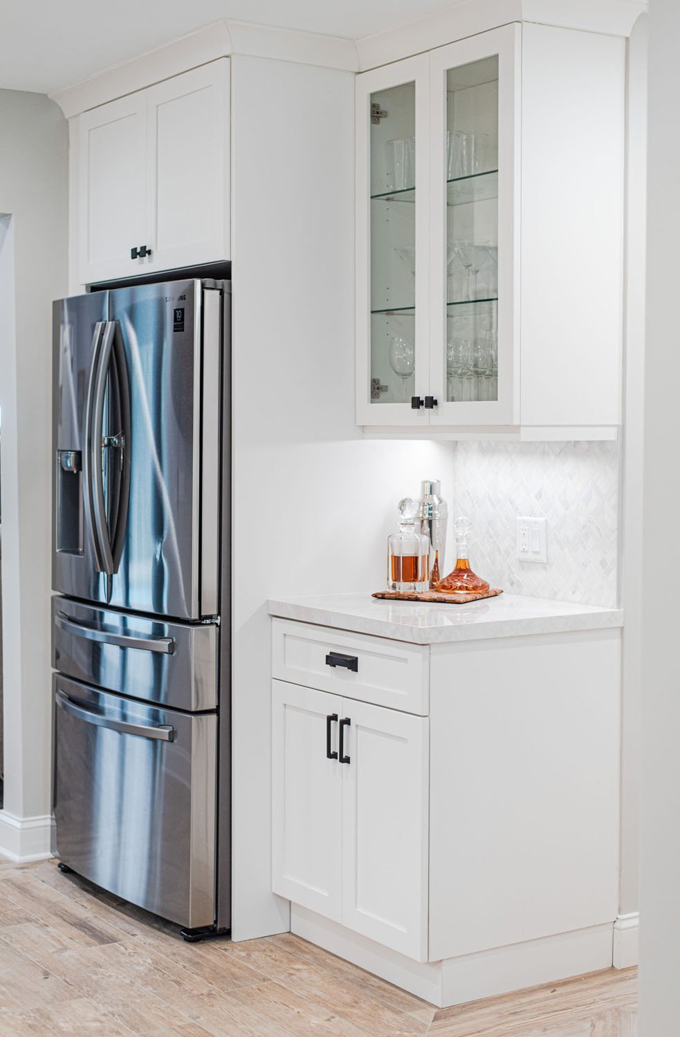 Refrigerator wall with stainless fridge and glass-front upper cabinets