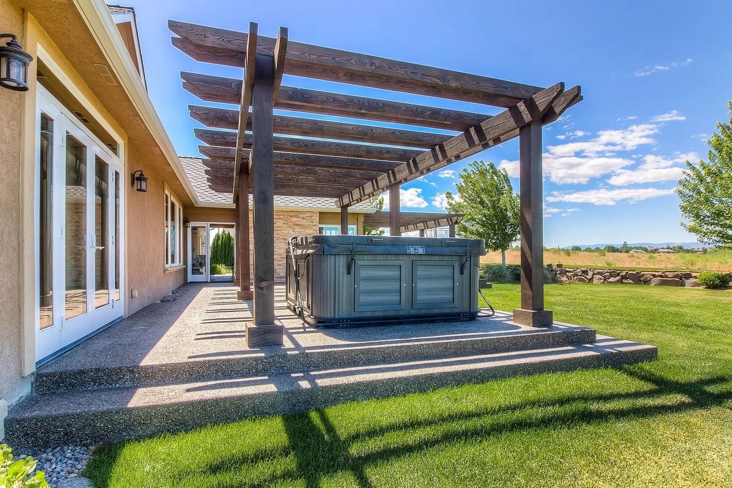 Pergola over a patio with hot tub beside the house
