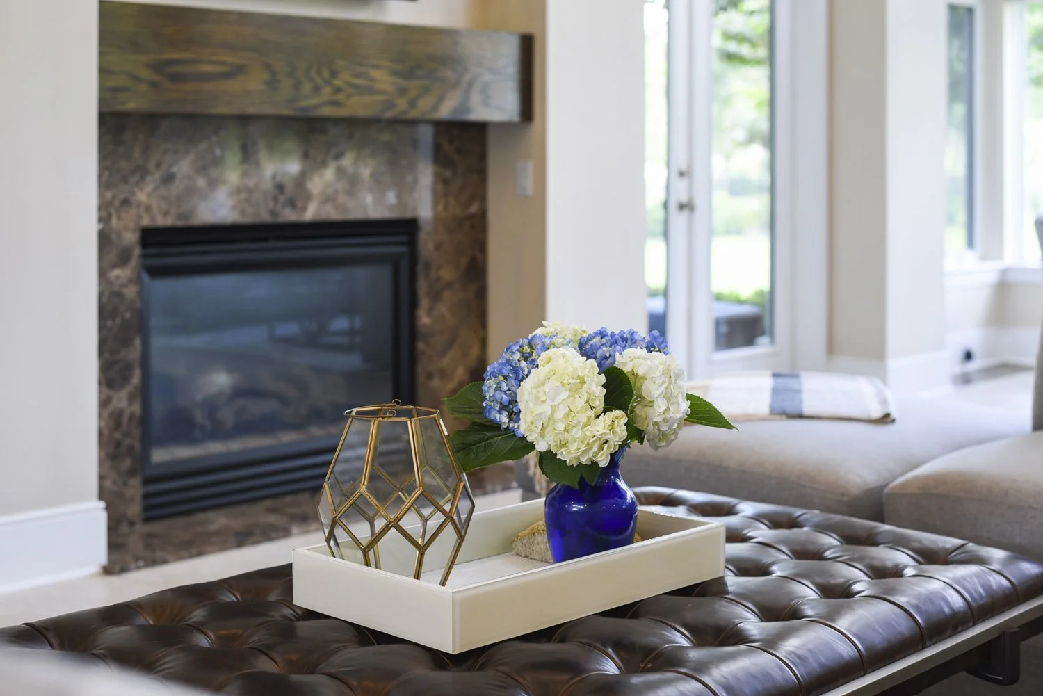 Stone fireplace with tufted leather ottoman and blue hydrangeas