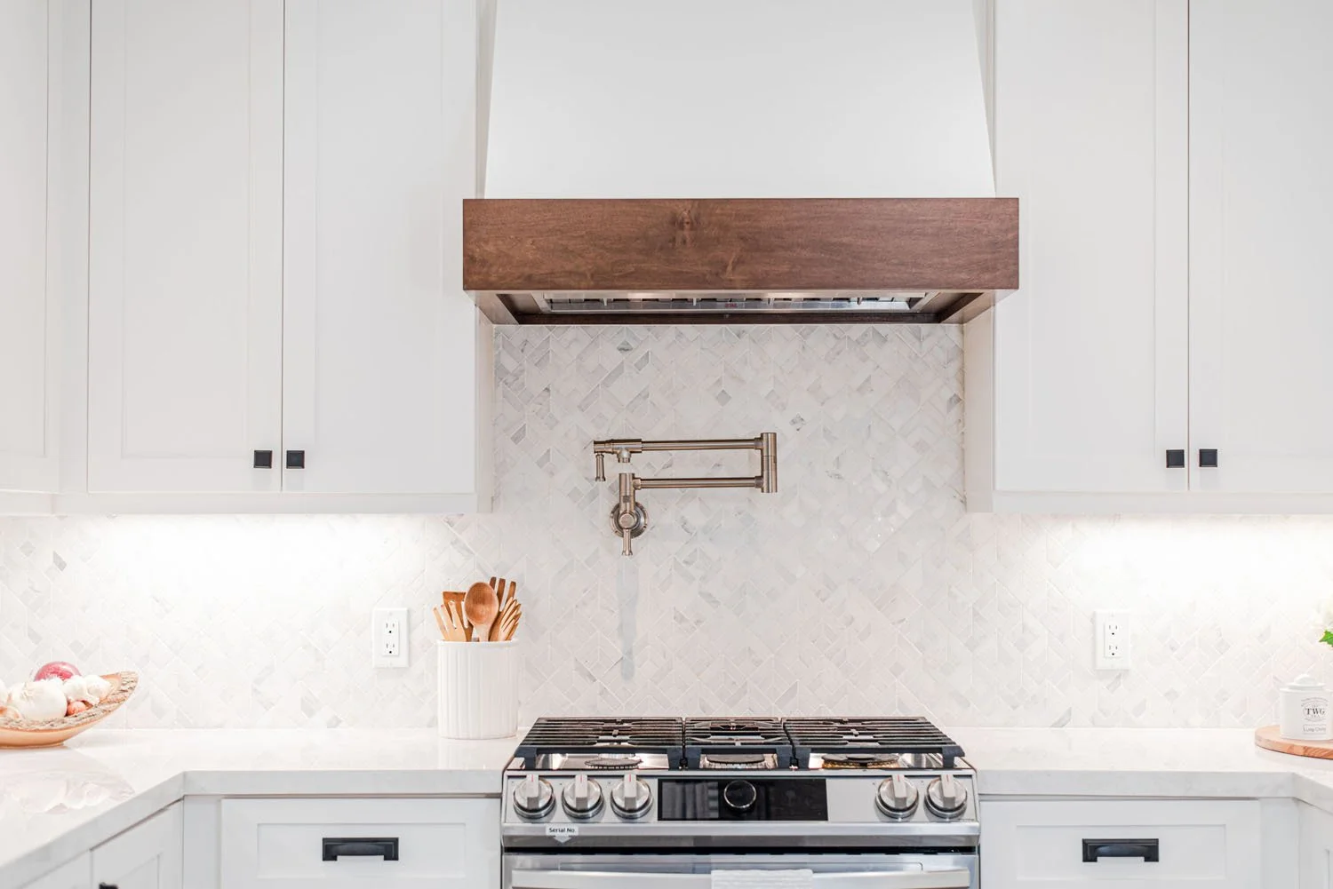 Range wall with white cabinets, walnut hood band and pot filler