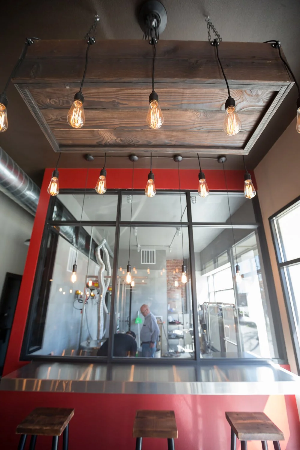 Glass-walled brewhouse with Edison pendants and red wall