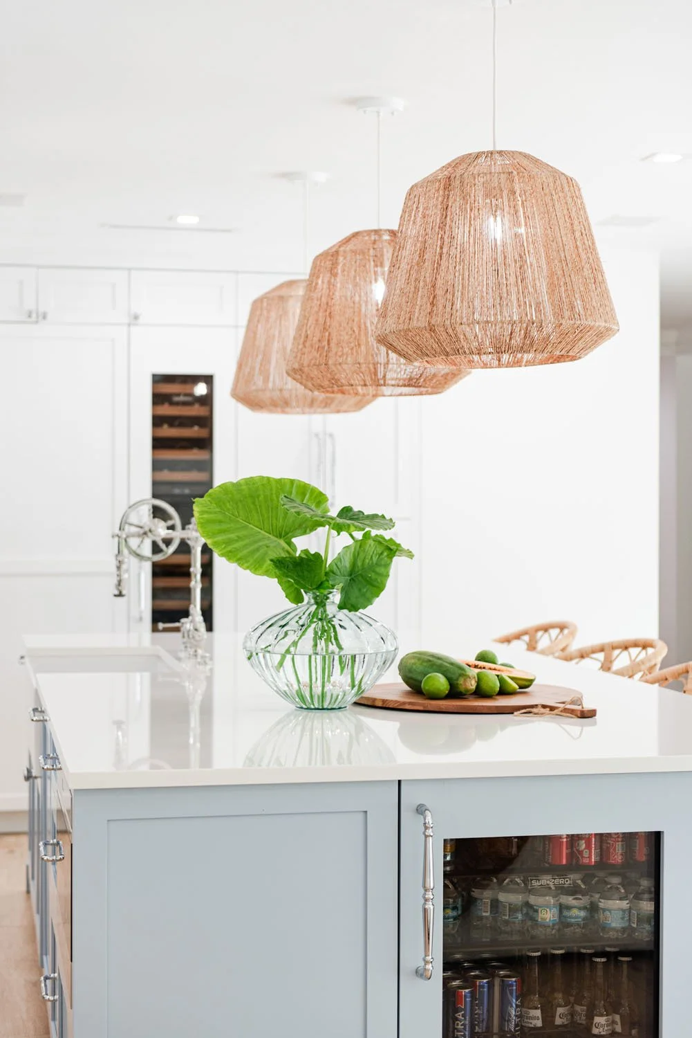 Light blue island with wine fridge under rattan pendants