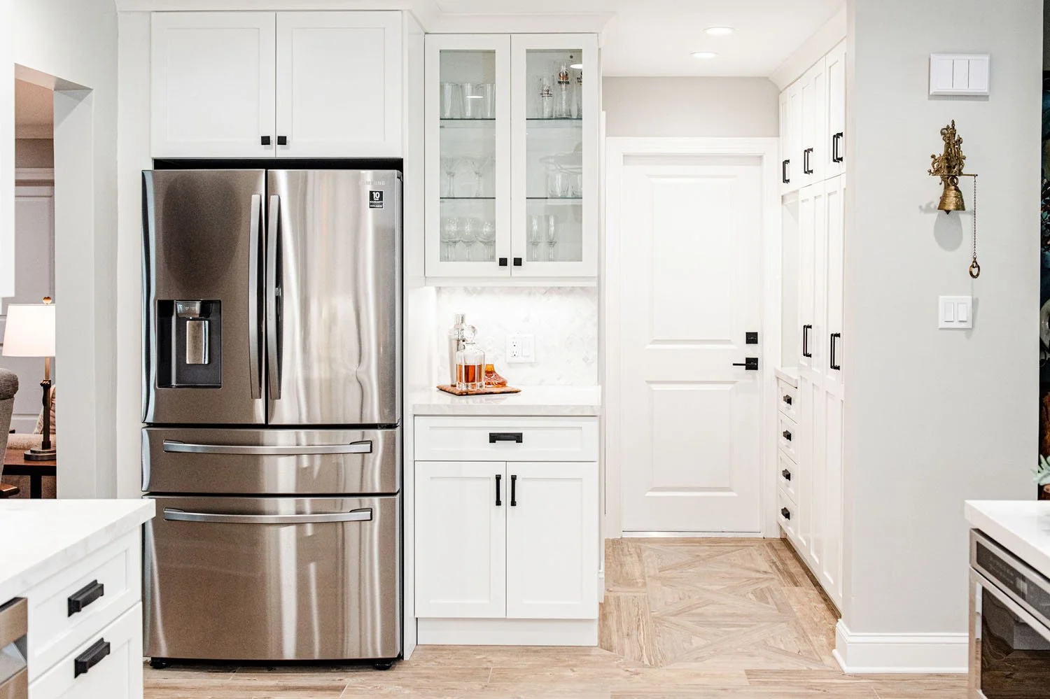 Stainless refrigerator beside glass-front cabinets and hallway door