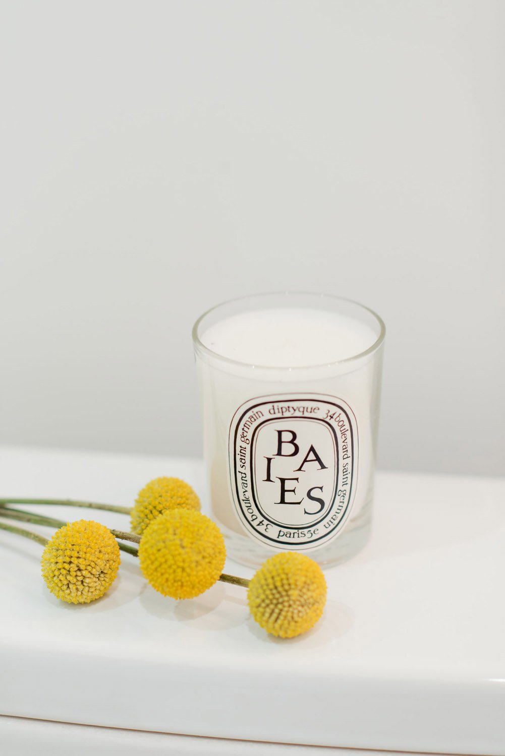 Candle and yellow billy button flowers on a white counter