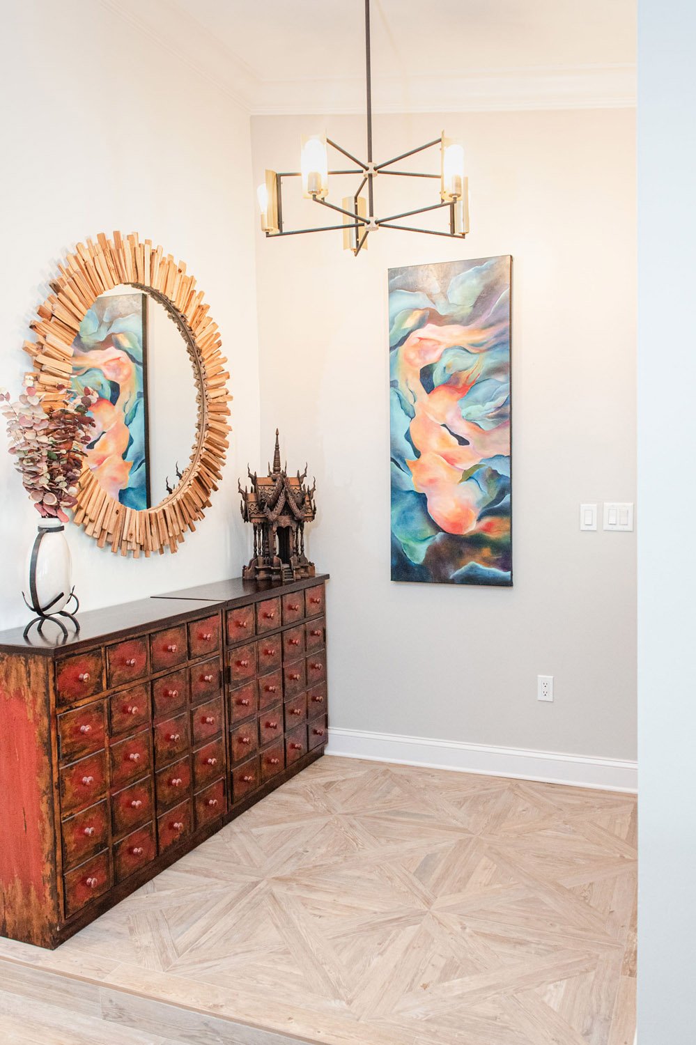Entry with carved wood chest, sunburst mirror and abstract art