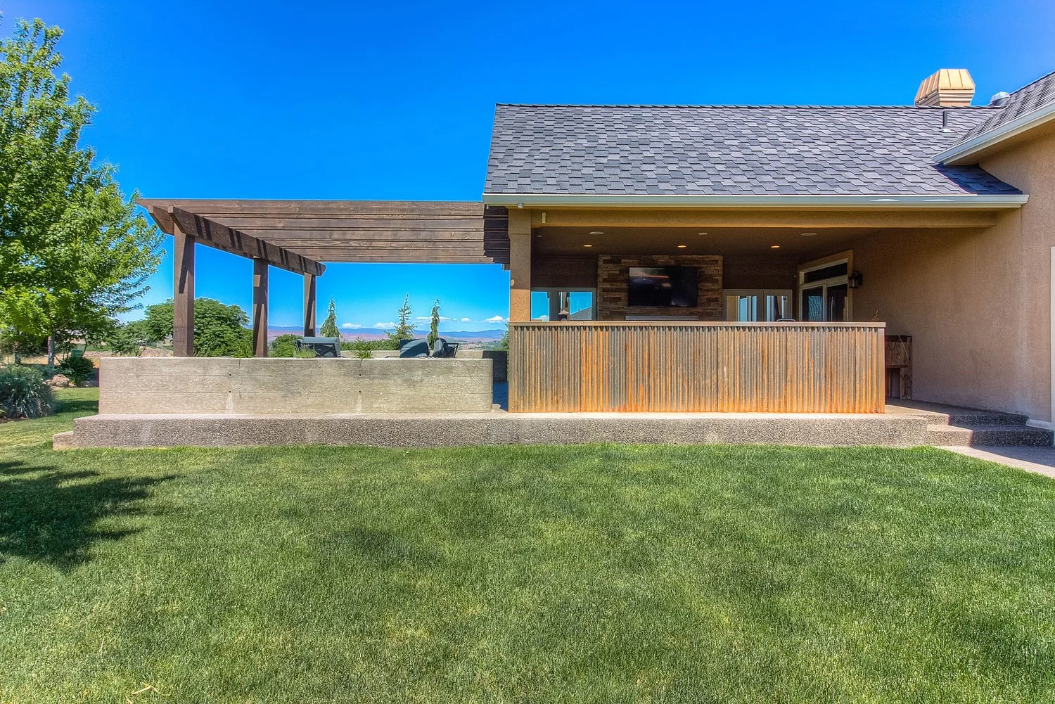 Backyard view of covered sunroom and wood pergola on a lawn