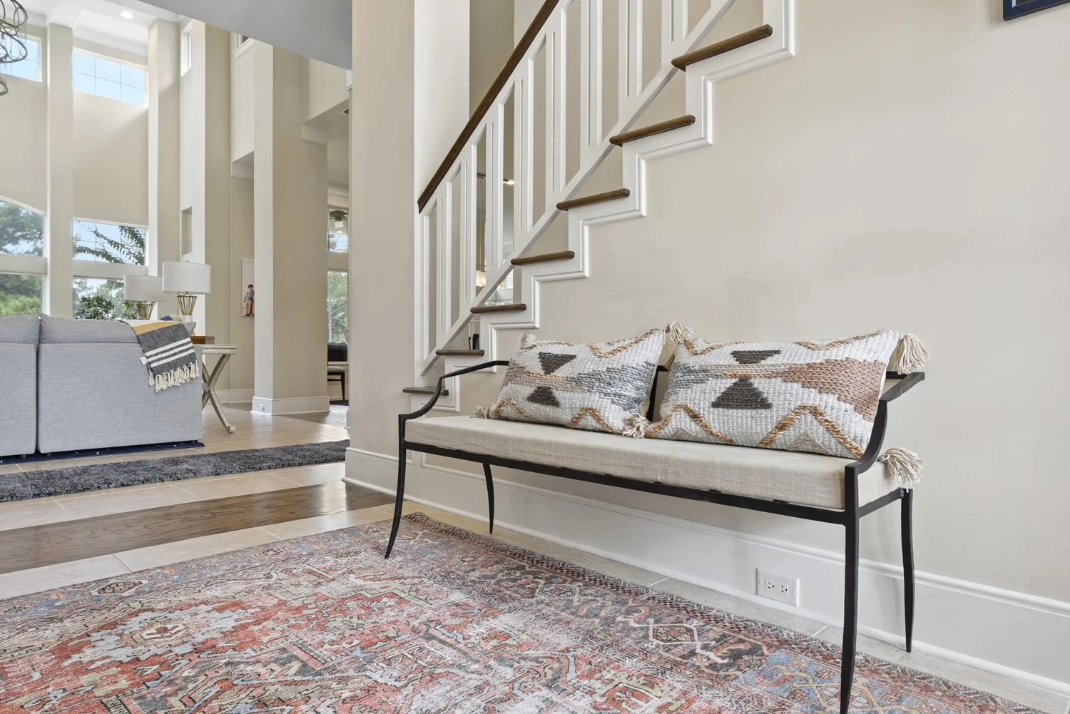 Upholstered bench with striped pillows under a white staircase