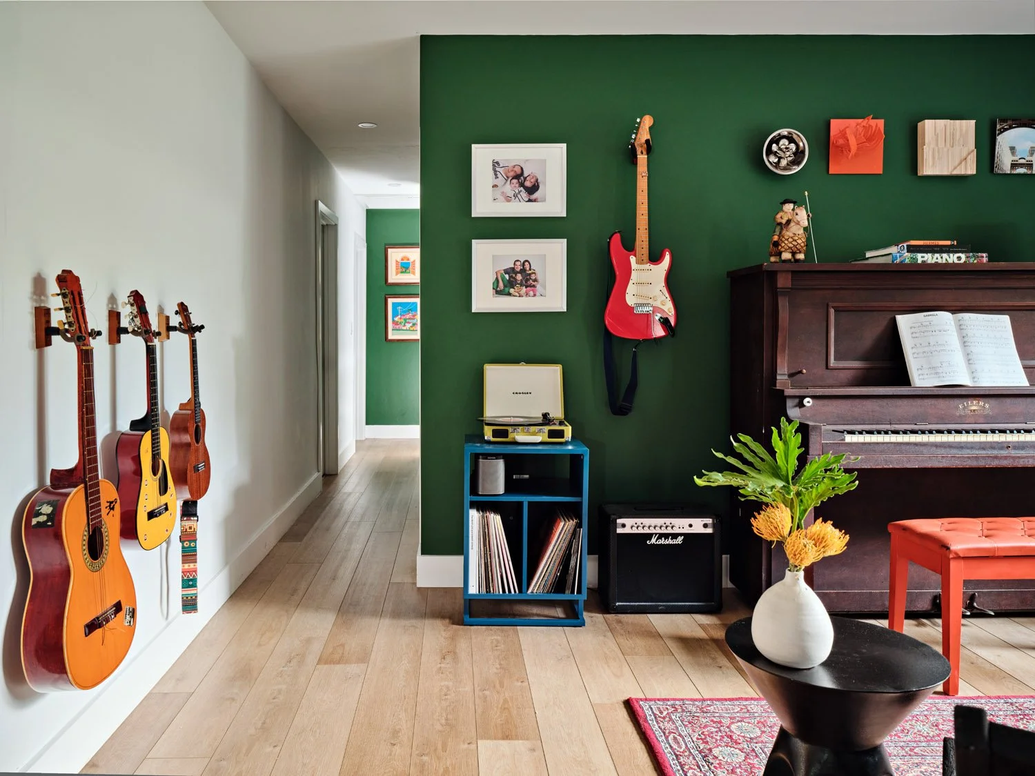 Guitars on the wall beside an upright piano and green accent wall