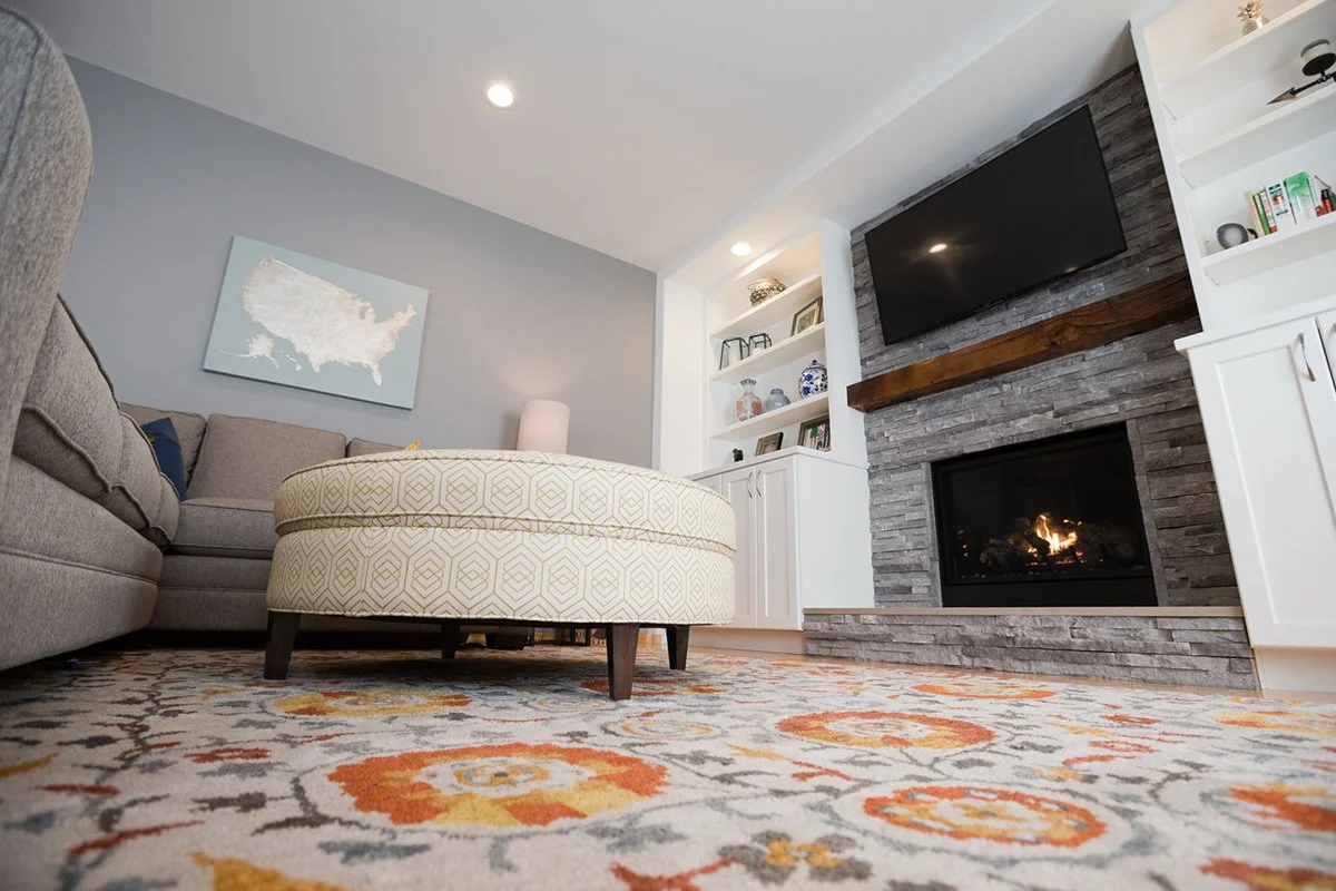 Round upholstered ottoman on a colorful rug by the fireplace
