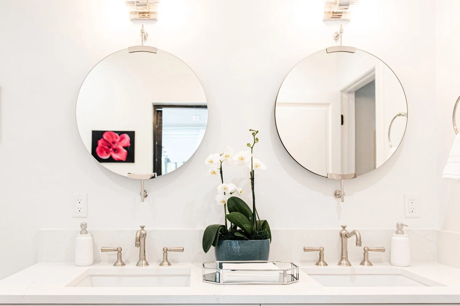 White double vanity with two round mirrors and orchid