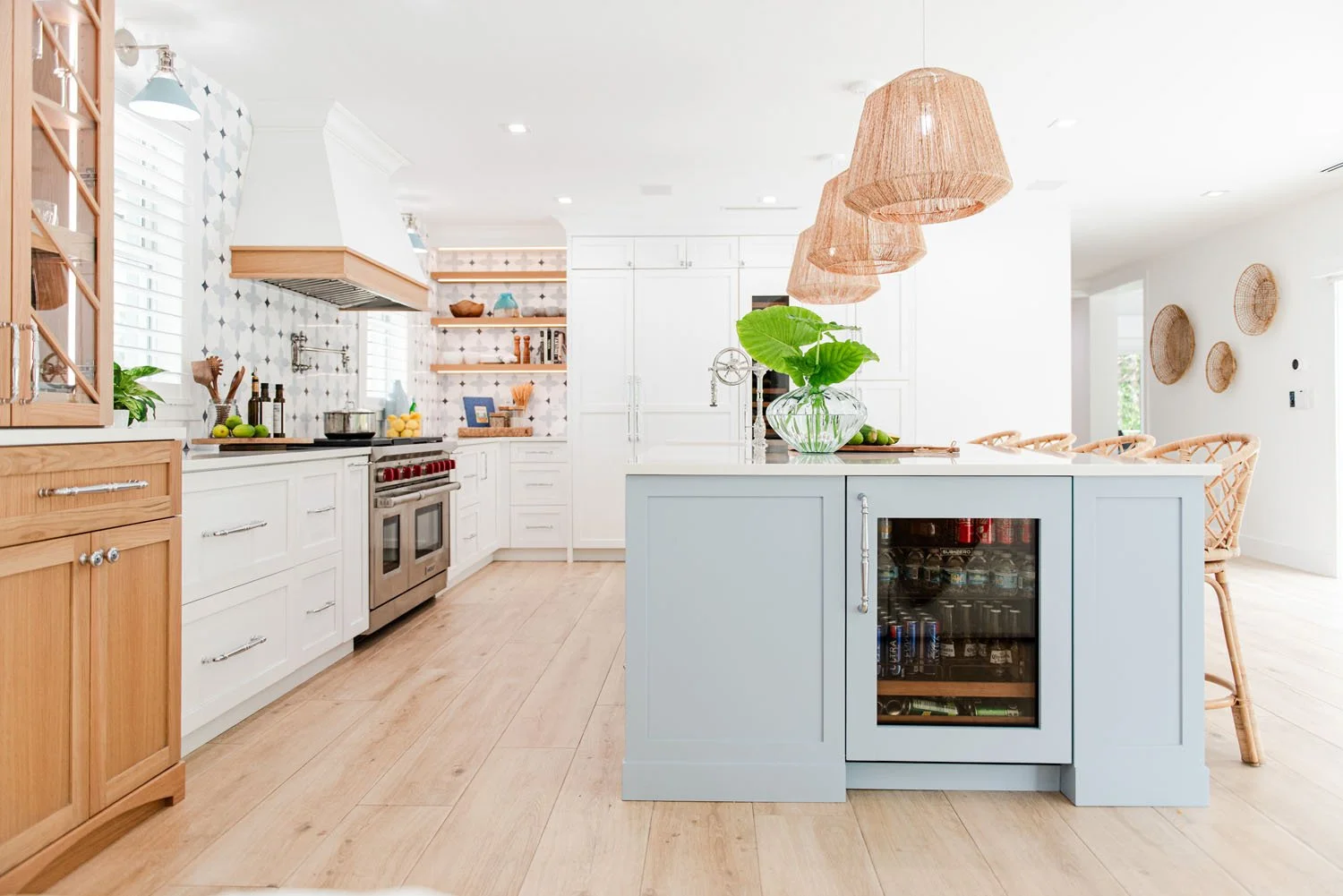 White kitchen with light blue island, rattan pendants and wood hutch
