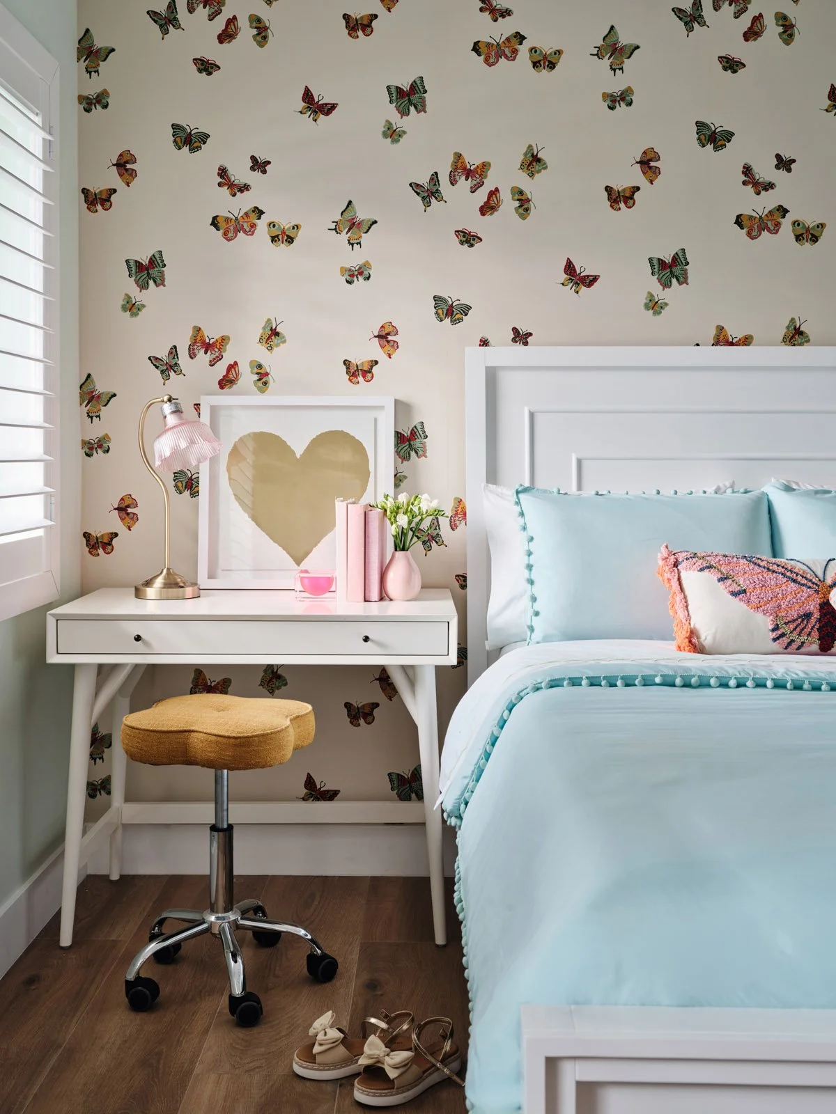 White desk with gold stool beside a bed with butterfly wallpaper