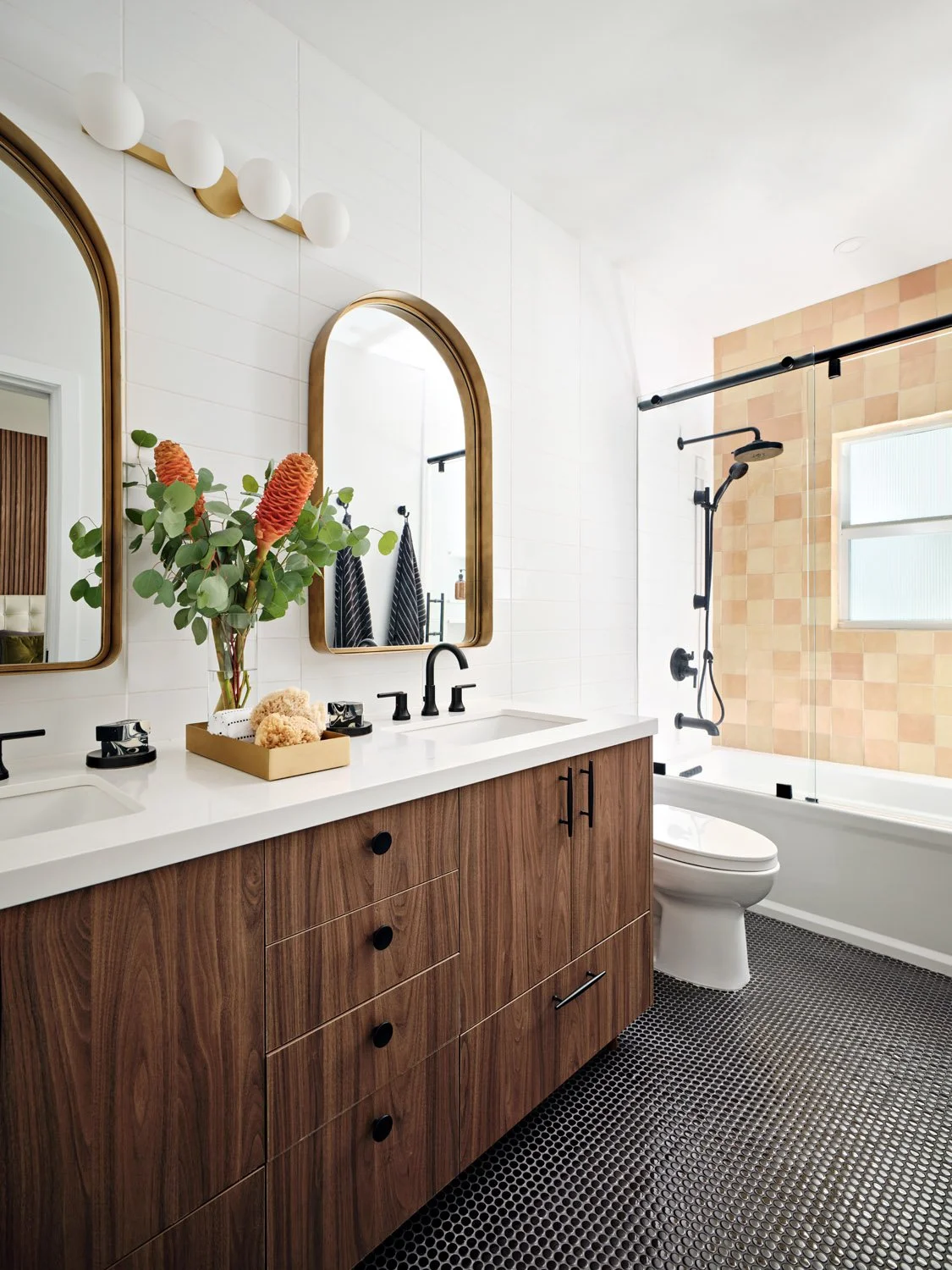 Bathroom with walnut vanity, arched brass mirror and black hex floor tile