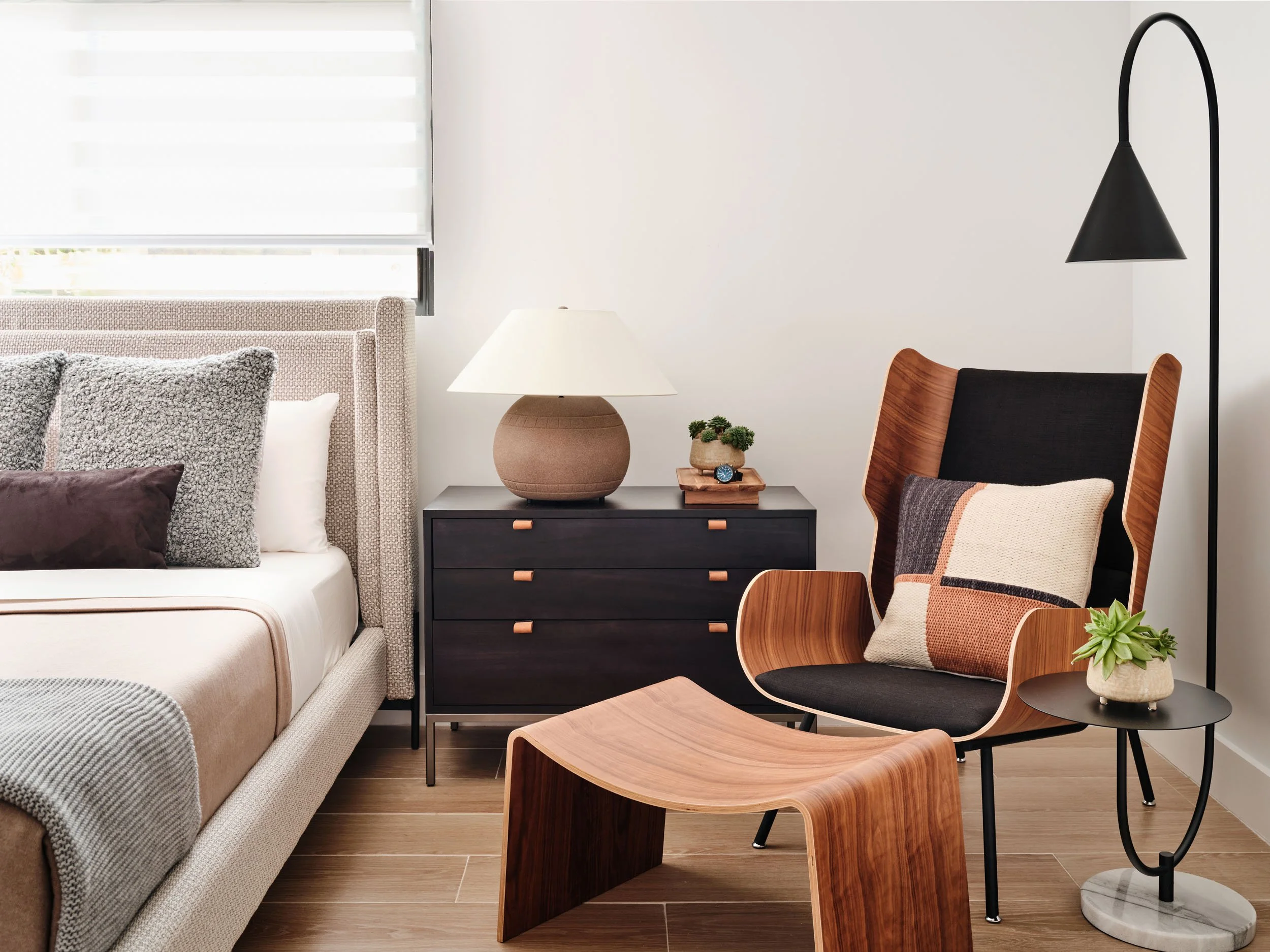 Bedroom with upholstered bed, black dresser, table lamp and leather lounge chair