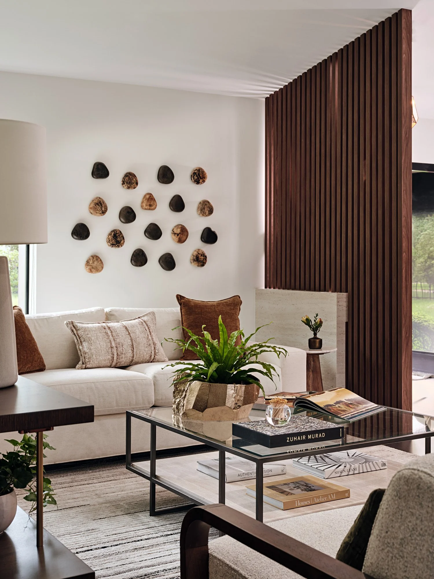 Glass coffee table with plant in front of cream sofa and wood wall sculptures