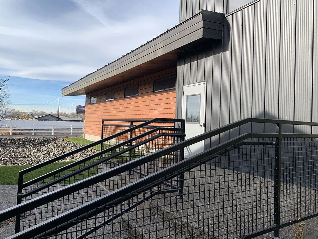Exterior ramp with black metal railing beside wood siding