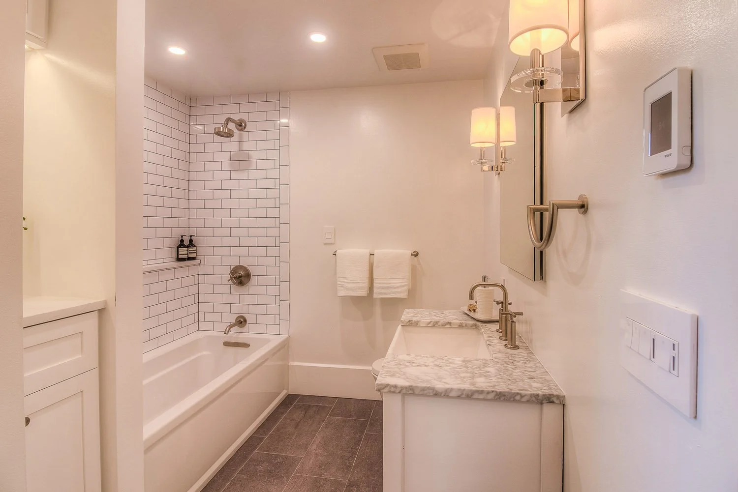 Bathroom with white tub, wall sconce and wood floor
