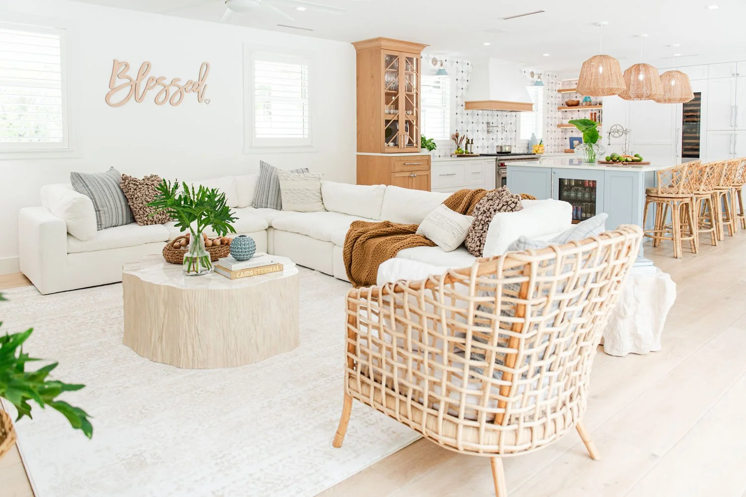 Open living room with white sectional, rattan chair and kitchen beyond