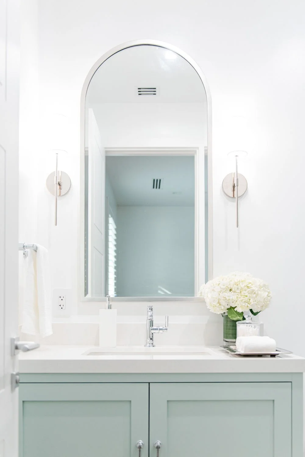 Sage green vanity with arched mirror and brass sconces