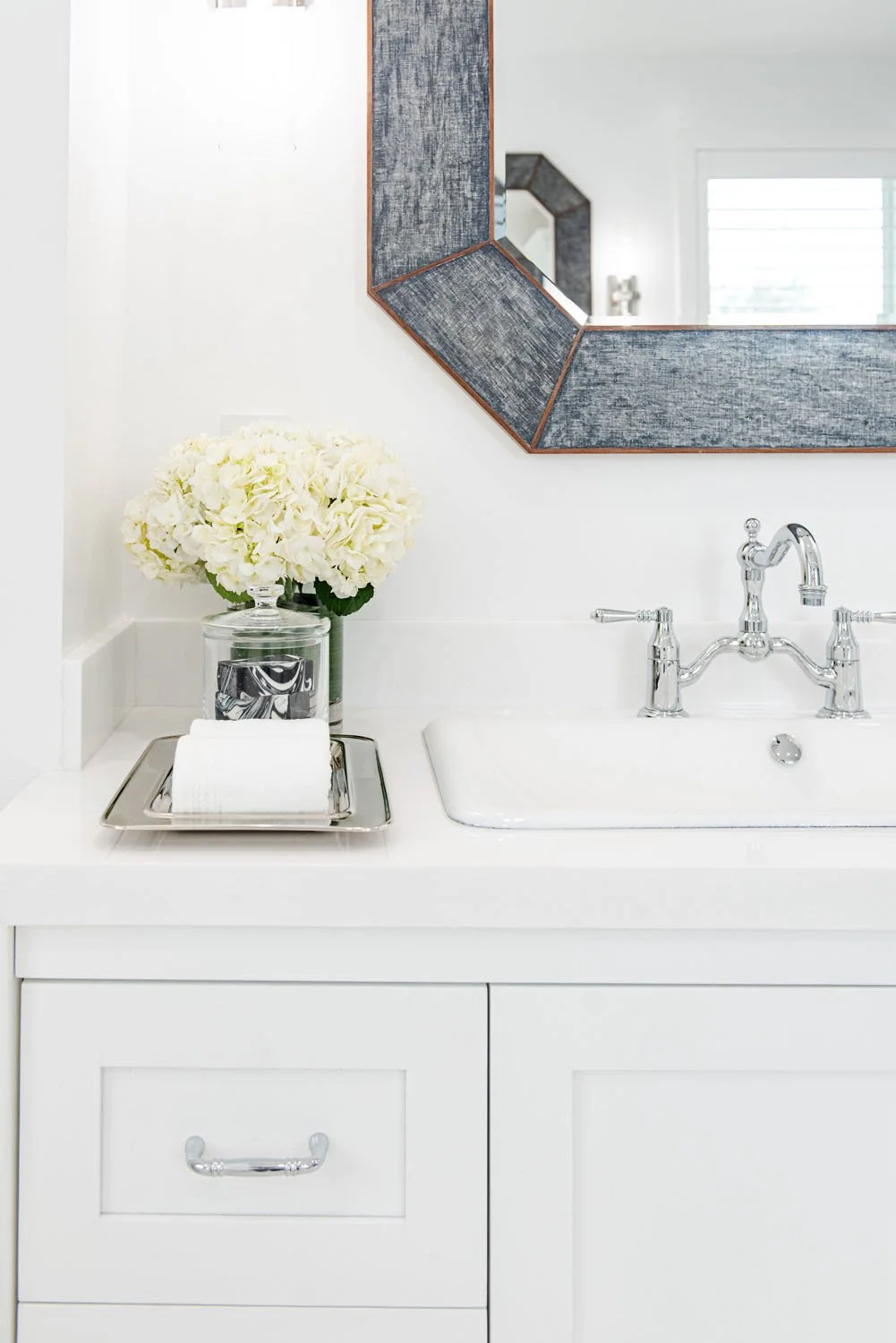 White vanity with gray framed mirror and white roses