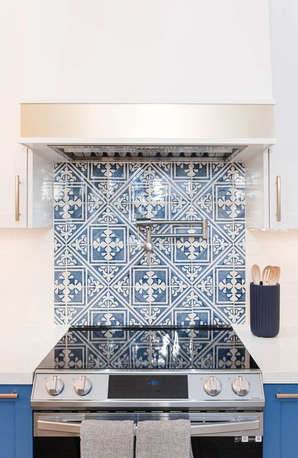 Stainless range under a white and brass hood with blue tile