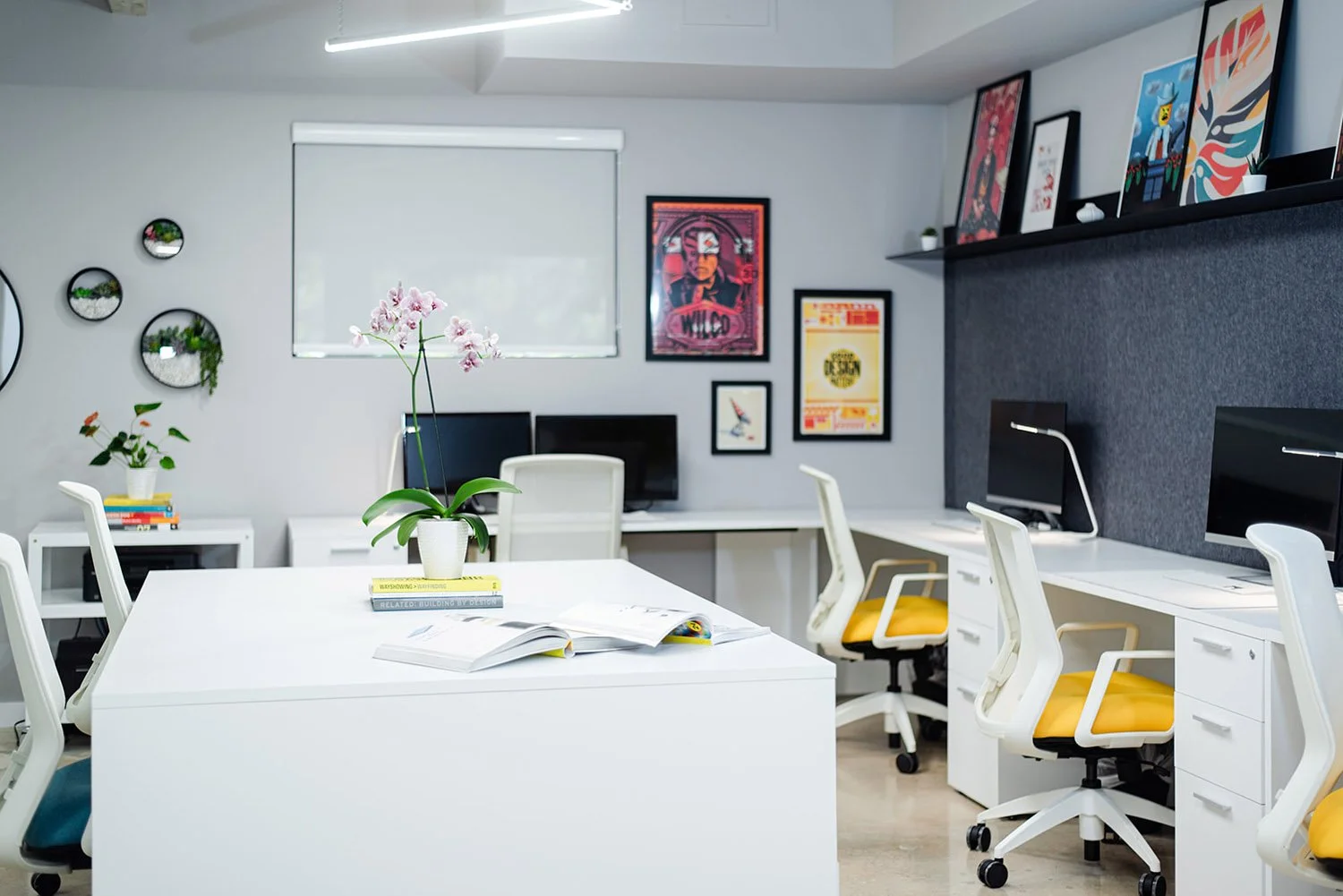 Open office with white desks, yellow chairs and framed posters