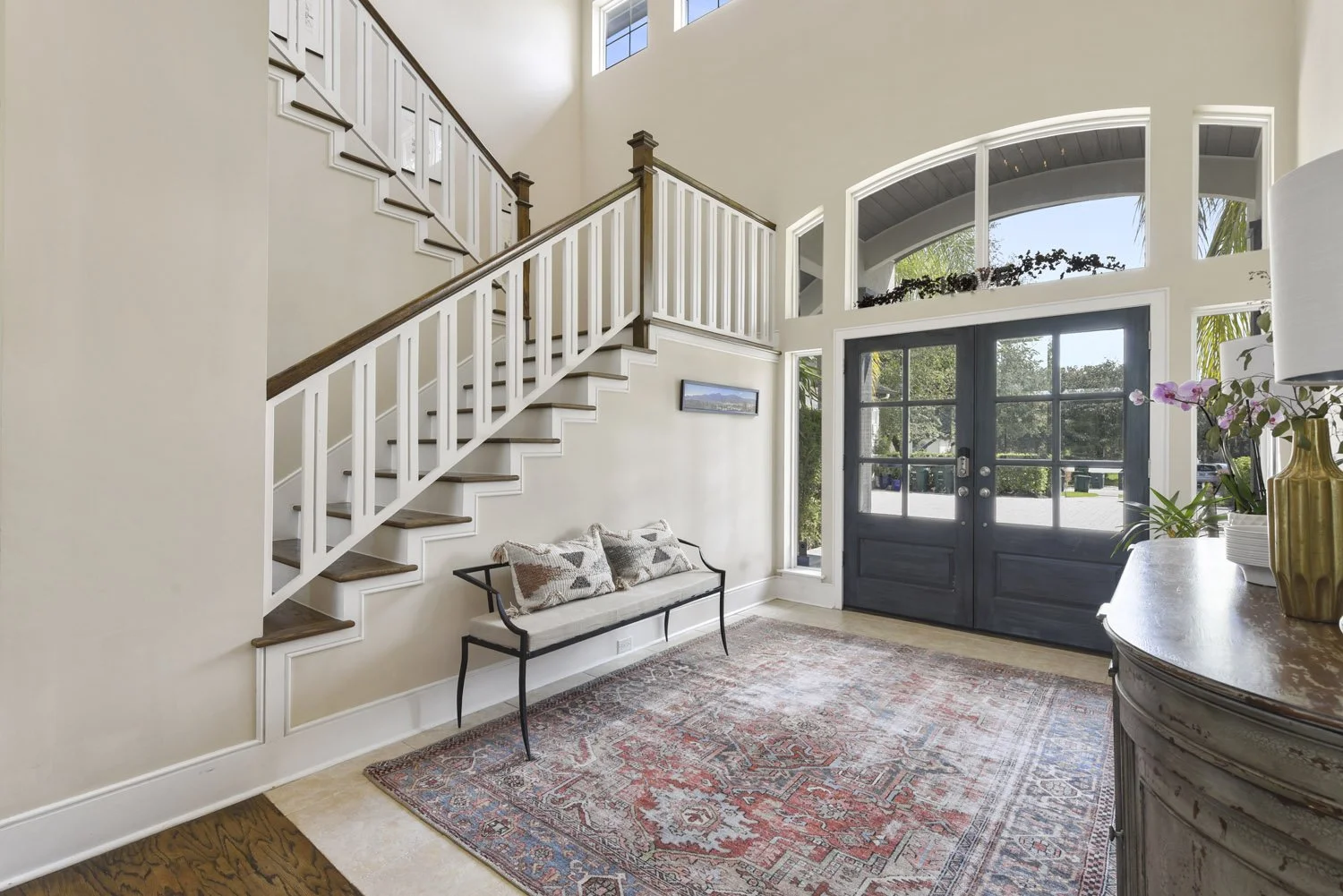 Foyer with curved staircase, black front doors and bench