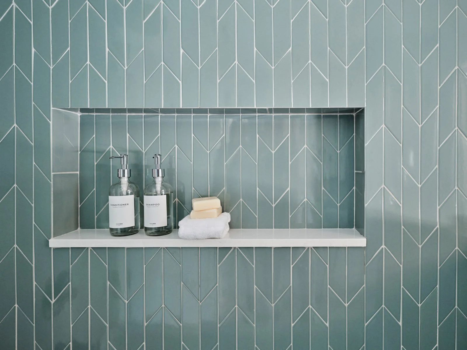 Green herringbone tile shower niche with toiletries