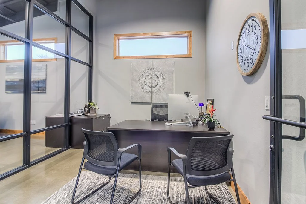 Glass-walled office with desk, chairs and wall clock