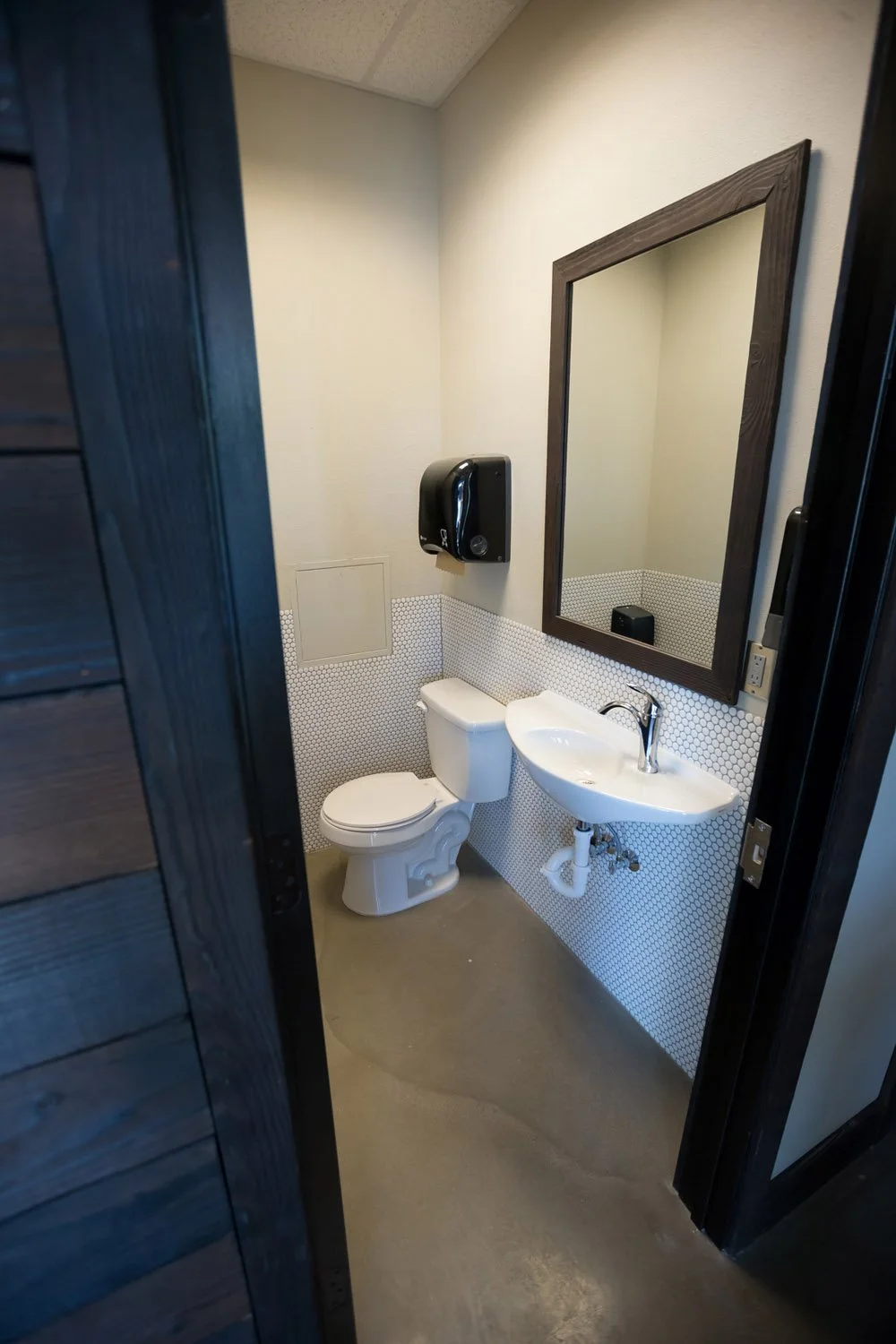 Restroom with dark wood door, wall sink and black mirror