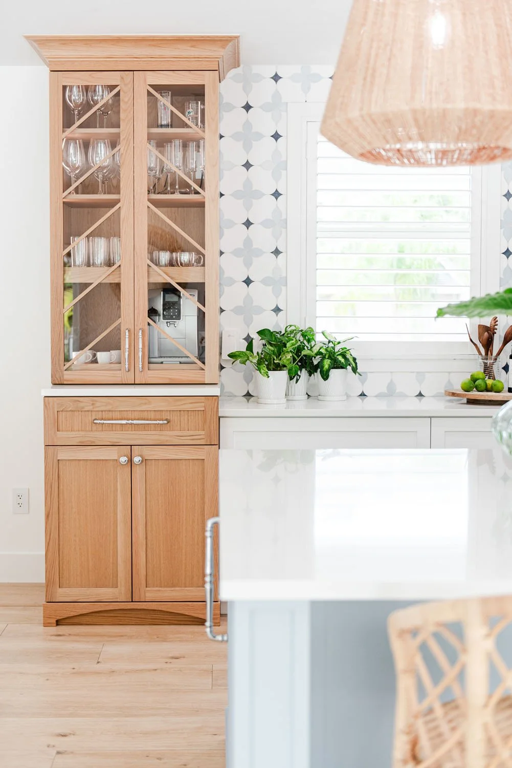 Light wood glass-front hutch beside patterned tile and rattan pendant