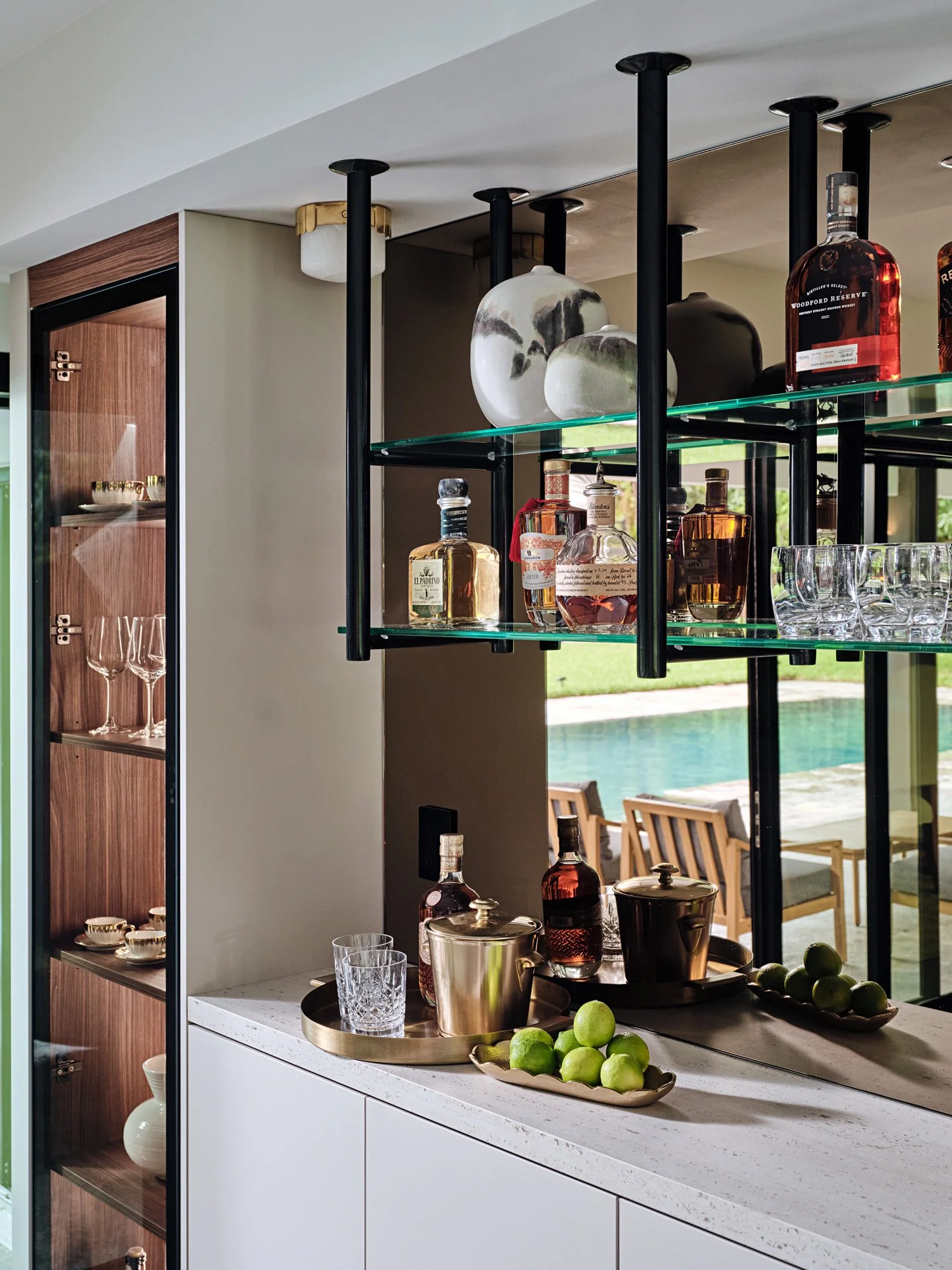 Bar cabinet with lit open shelving, glassware and pool view
