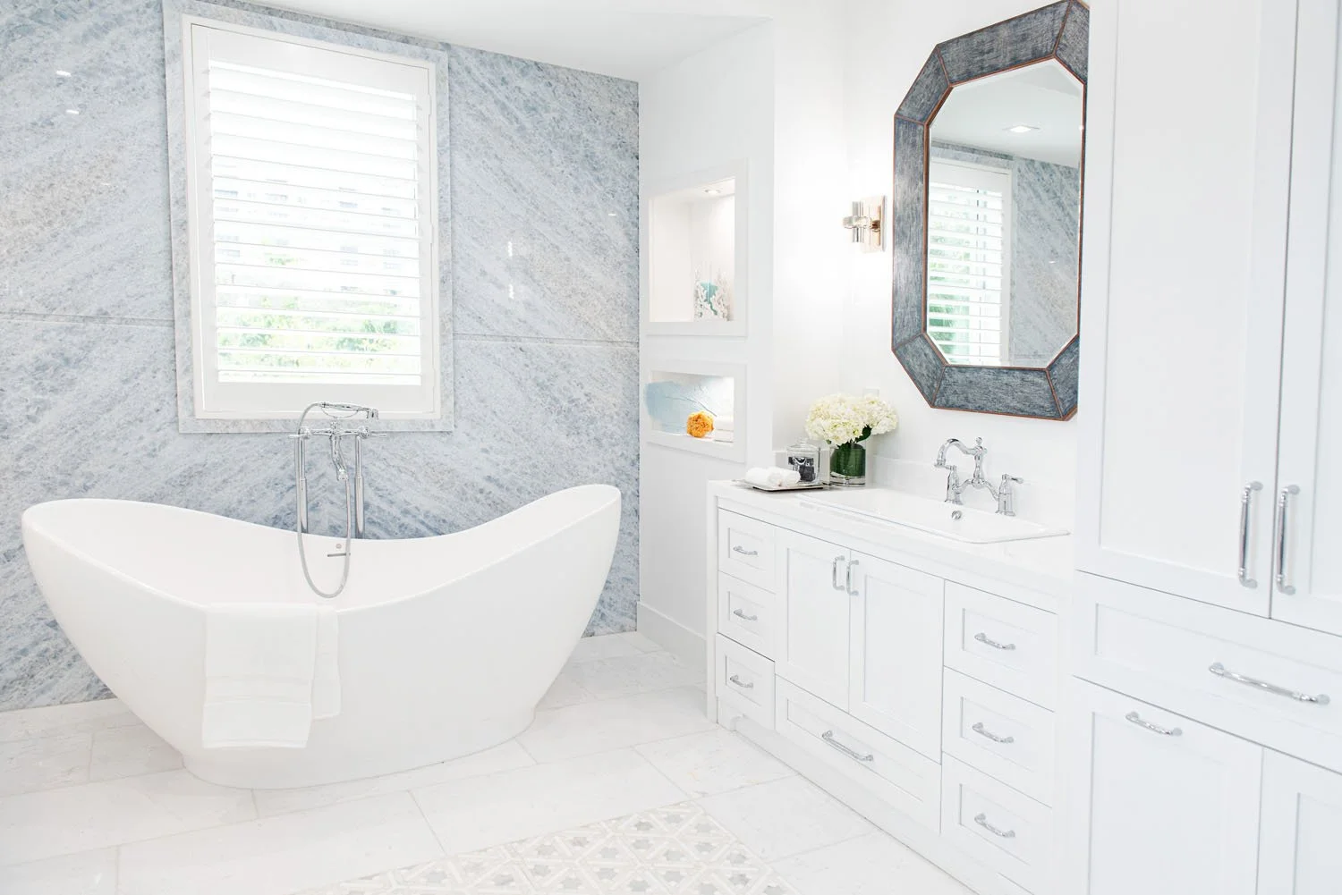 Freestanding tub beside a marble wall and white vanity