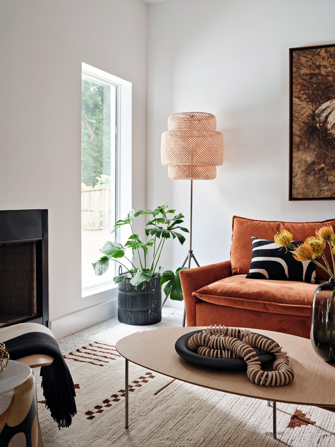 Rust velvet sofa beside a fireplace with rattan floor lamp and fiddle leaf plant