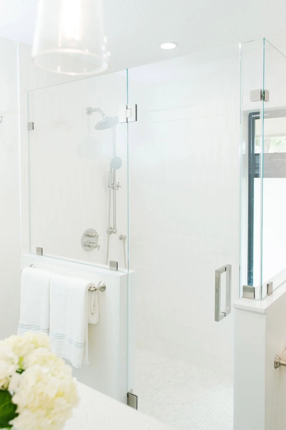 Glass shower with white tile and white hydrangeas