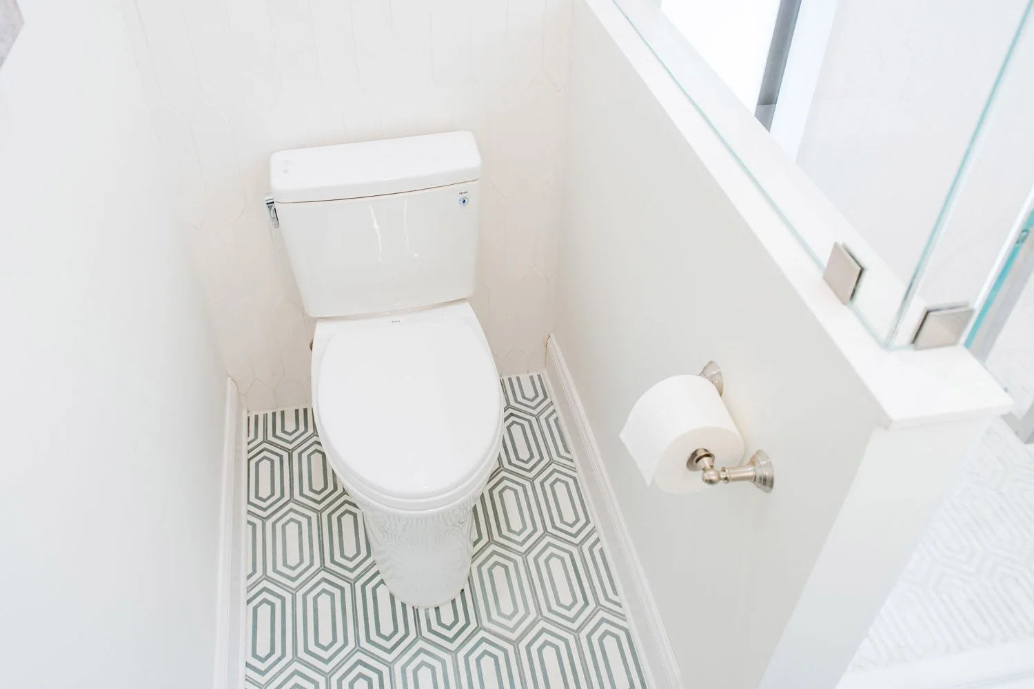 Toilet beside a half wall with geometric floor tile