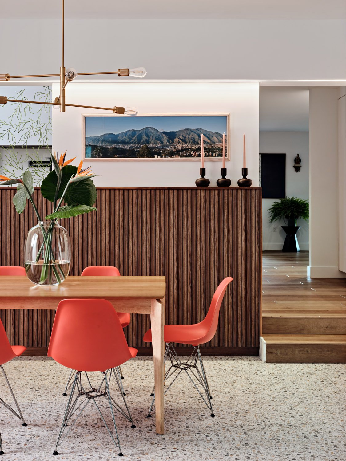 Wood dining table with coral chairs in front of a wood slat divider