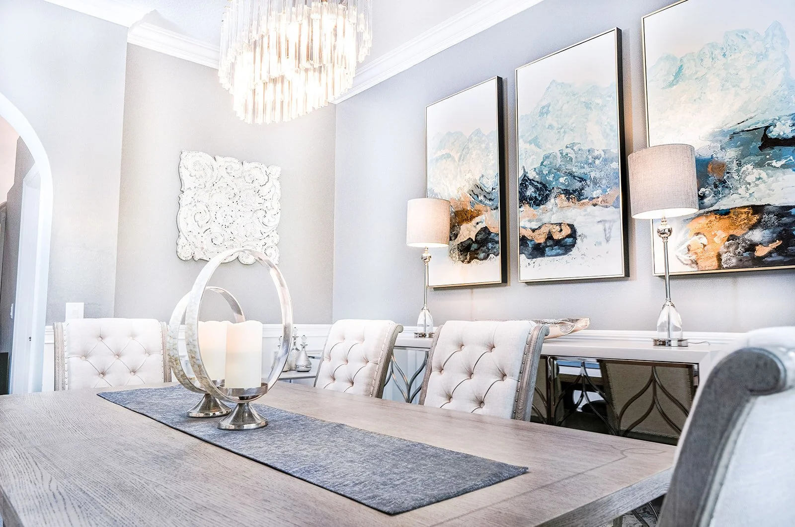 Dining table with tufted chairs beneath three blue abstract paintings