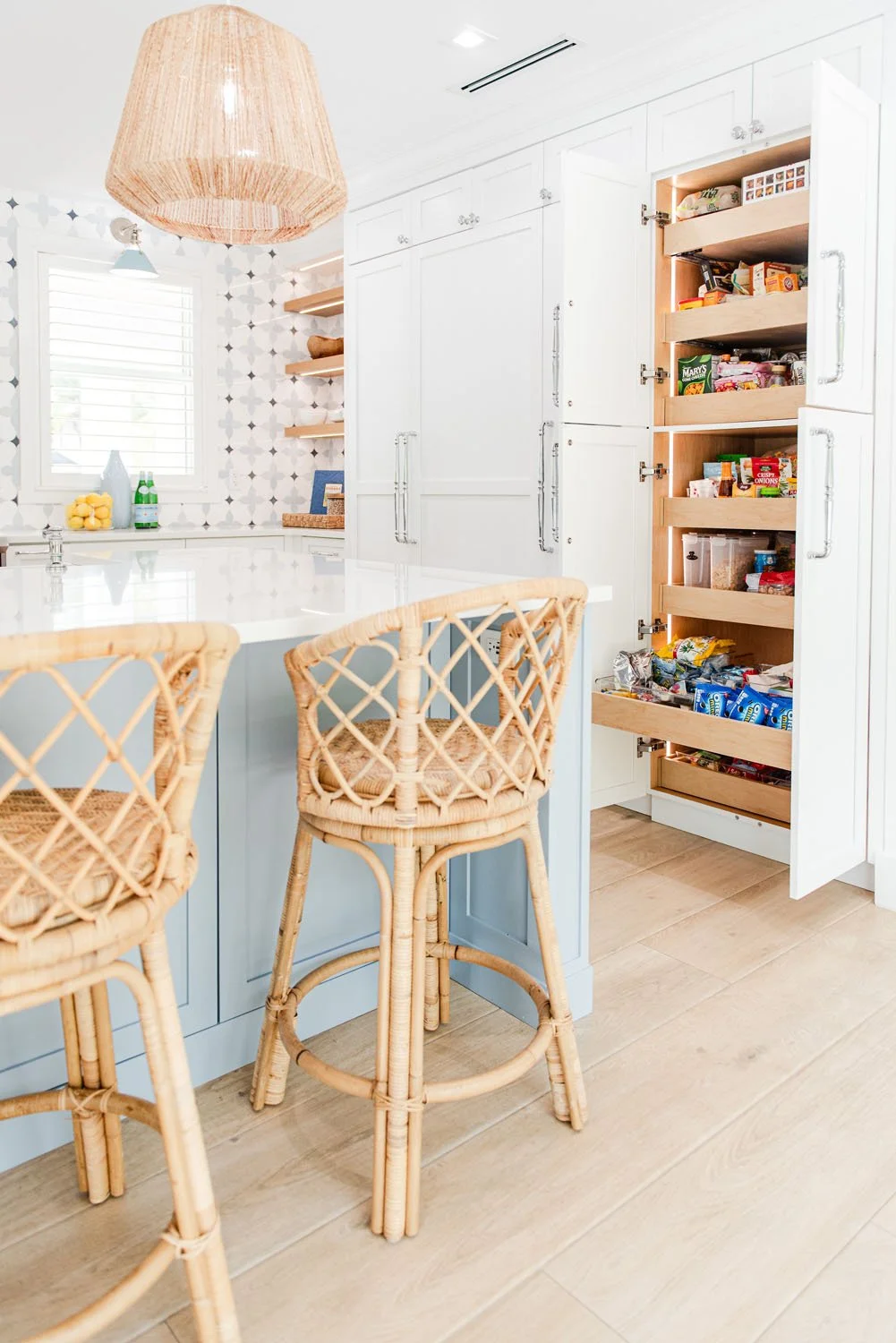 Rattan counter stools at a light blue island with pull-out pantry