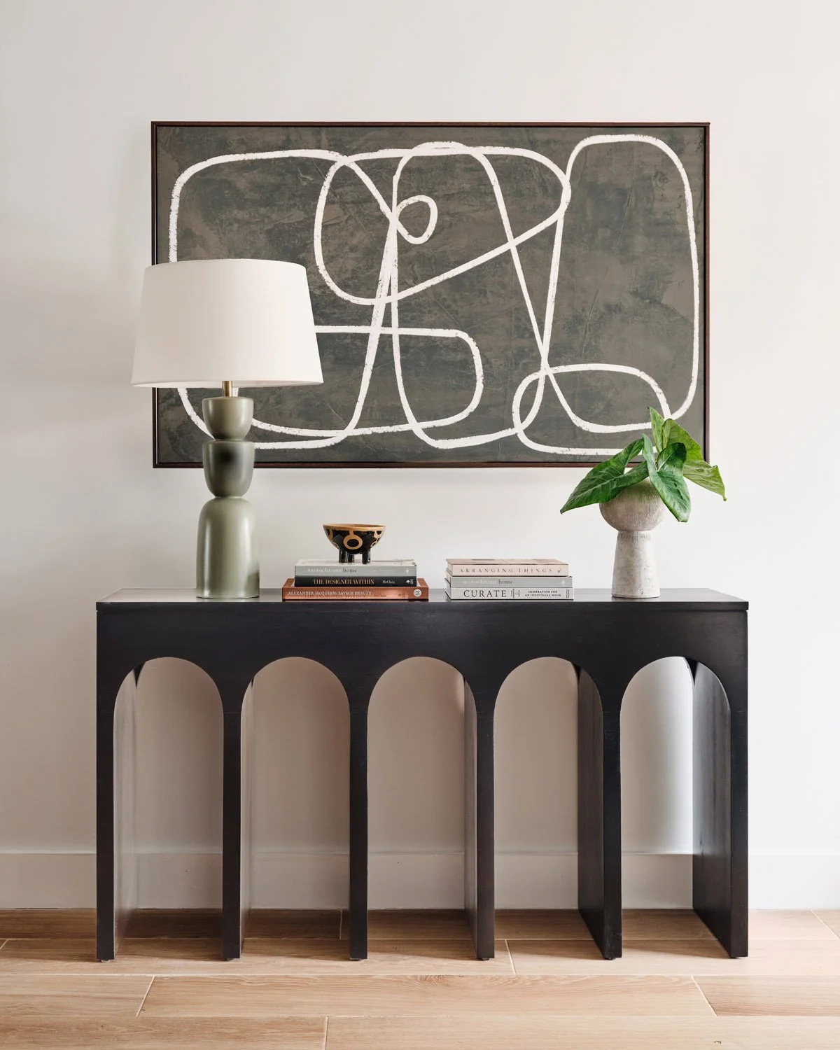 Black arched console table with table lamp and abstract artwork