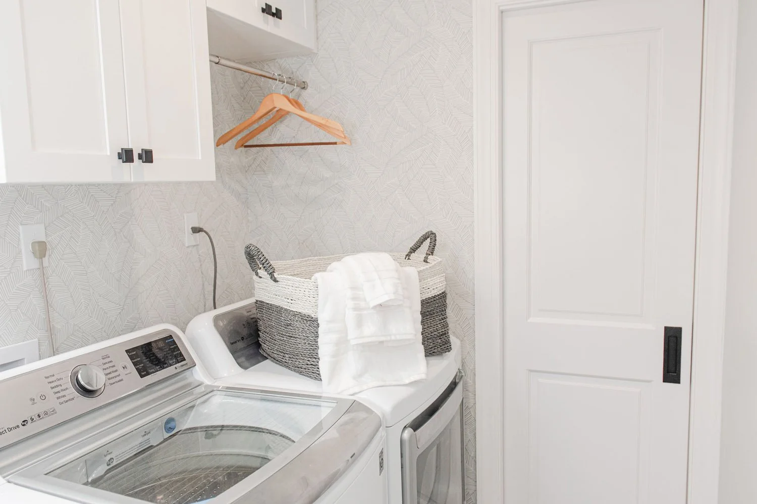 Top-load washer beside white cabinets and hanging rack